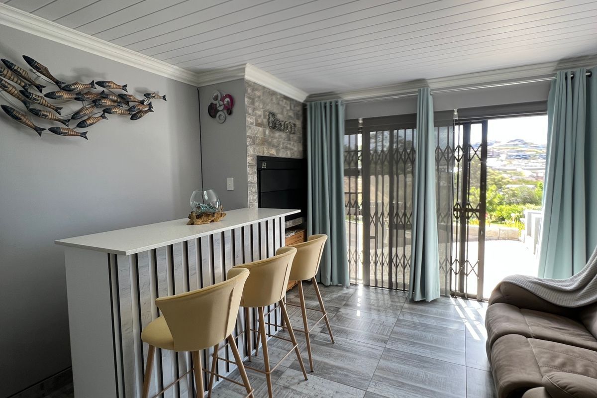 A well-maintained living area featuring a built-in bar, tiled flooring, decorative ceiling paneling, and sliding glass doors leading to an outdoor space.