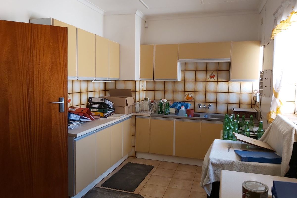 A dated kitchen featuring original cabinetry, tiled splashbacks, and a double basin sink, offering potential for a modern renovation.