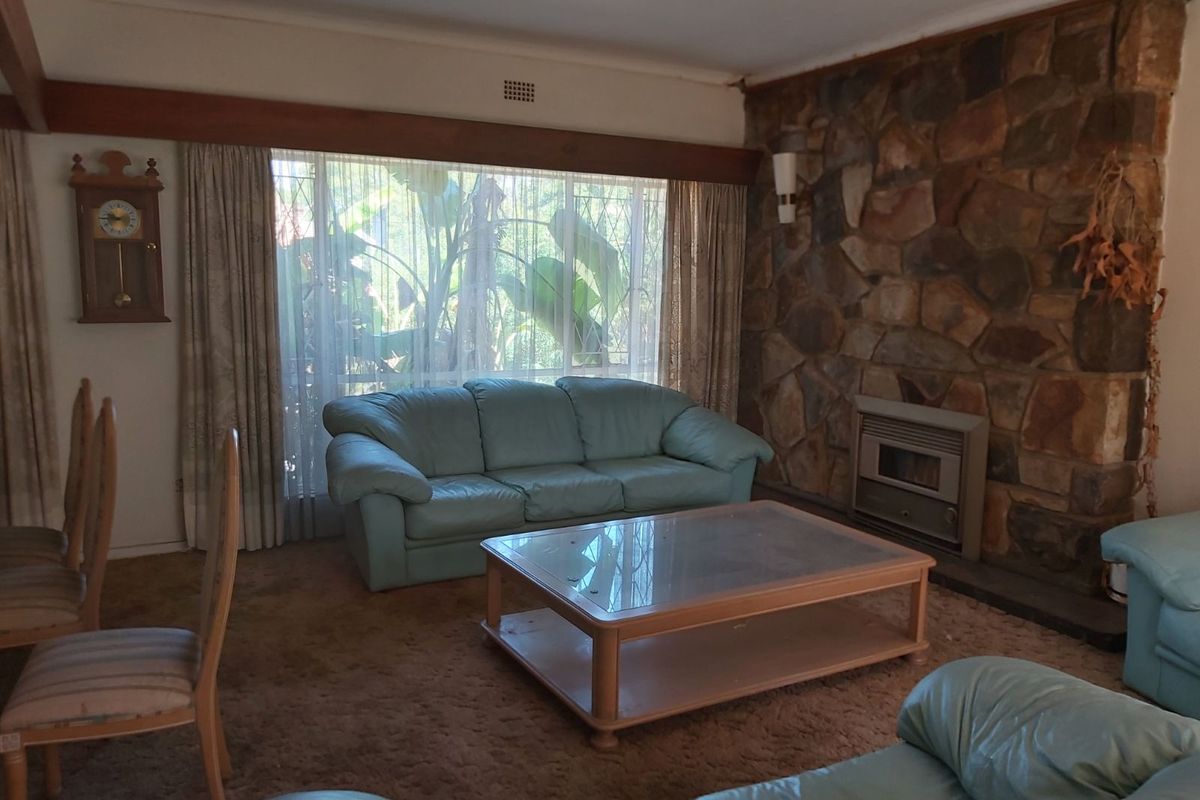 Spacious living room featuring a prominent natural stone fireplace, large window with garden views, and carpeted flooring.