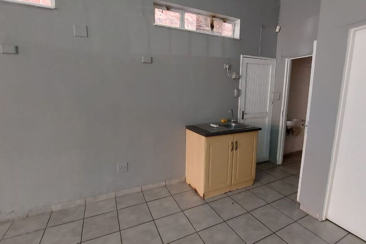 A small office kitchenette area featuring a single base cabinet with a sink, tiled flooring, and access to an adjacent restroom.