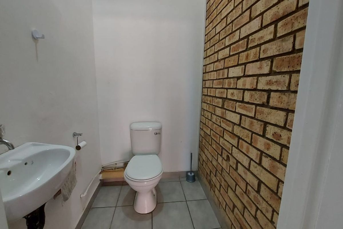 A functional office restroom featuring a toilet, wall-mounted basin, and a decorative exposed brick feature wall.