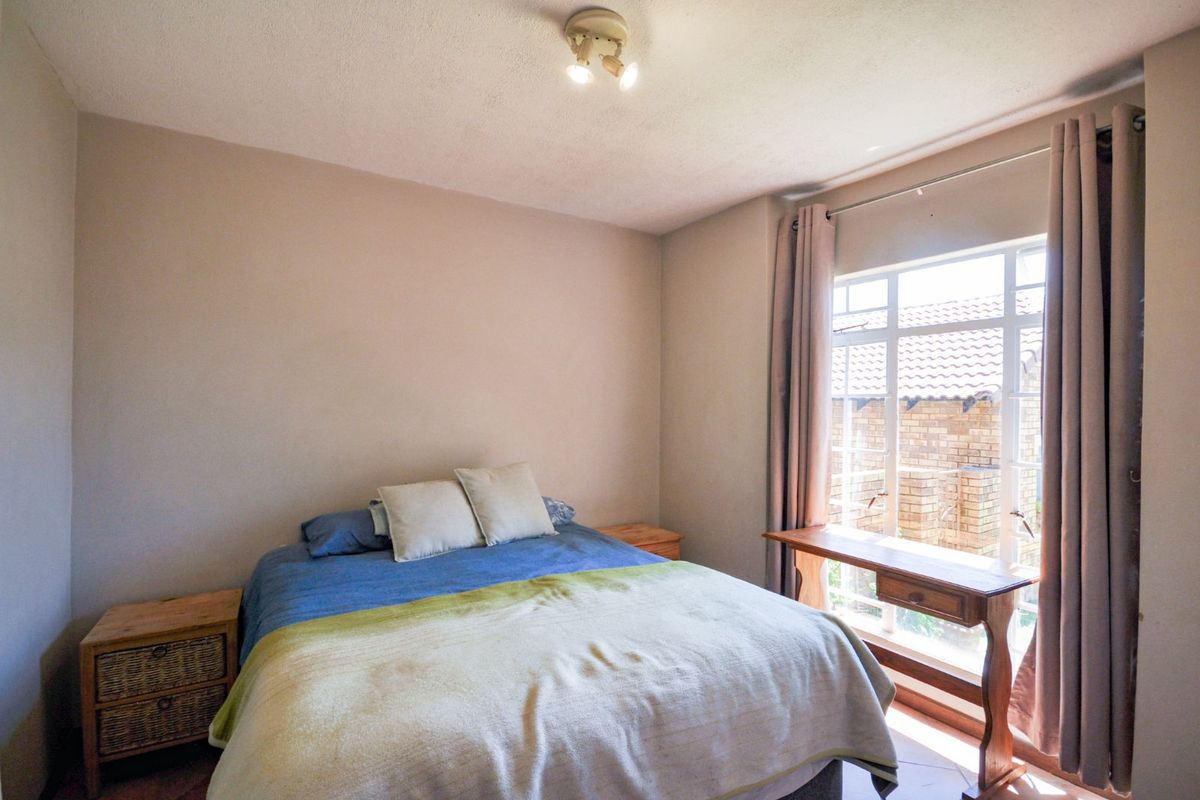 A functional bedroom featuring a large window with natural light, neutral wall tones, and a standard ceiling-mounted light fixture.