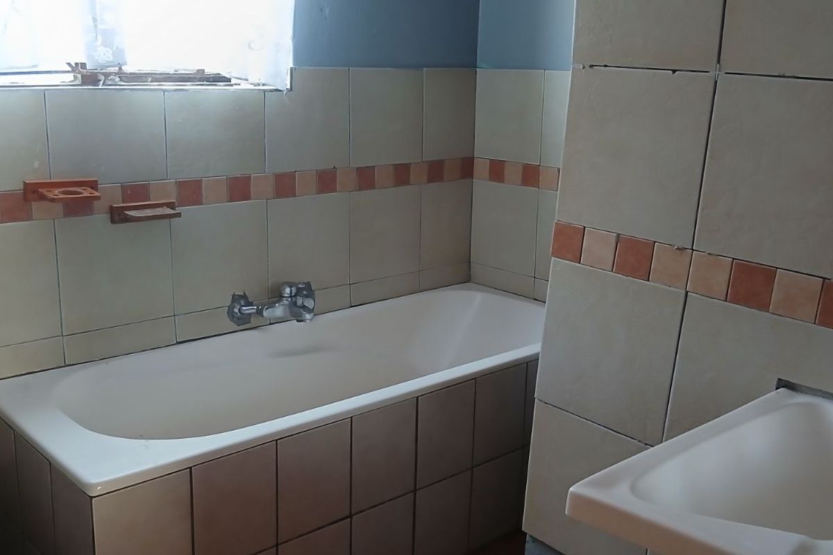 A dated bathroom featuring a built-in bathtub, wall-mounted basin, and toilet, requiring cosmetic updates and maintenance to the tiling and fixtures.