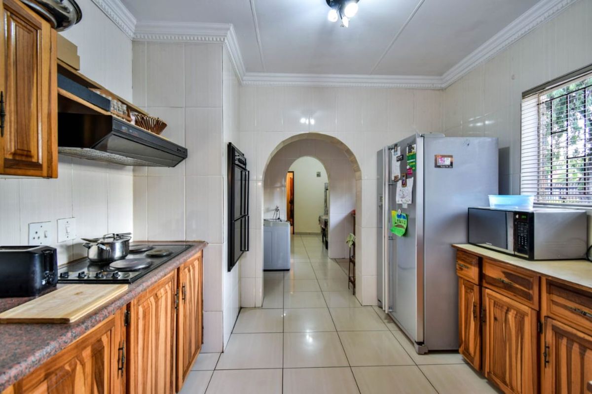 A functional kitchen featuring wooden cabinetry, built-in oven, extractor fan, and tiled flooring, leading through an arched doorway to the rest of the home.