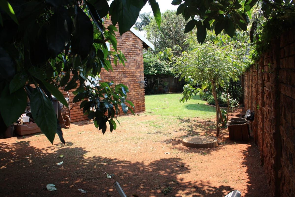 A private rear garden featuring a brick exterior wall, established trees, and a lawn area enclosed by a perimeter brick wall.