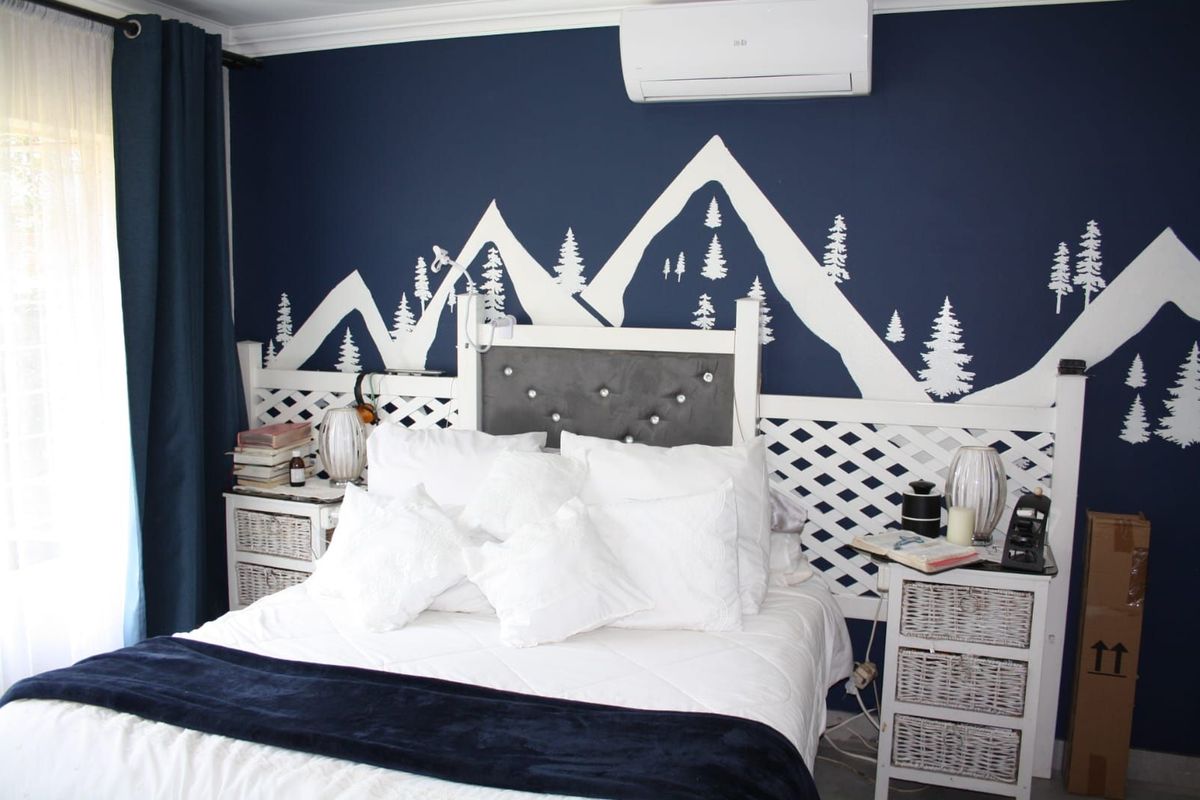 A bedroom featuring a dark blue accent wall with a mountain mural, crown molding, and a wall-mounted air conditioning unit.