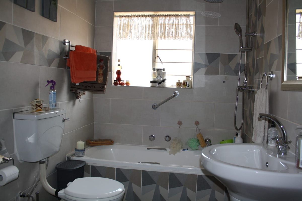 A functional bathroom featuring a bathtub with shower attachment, pedestal basin, and toilet, finished with patterned wall tiling.