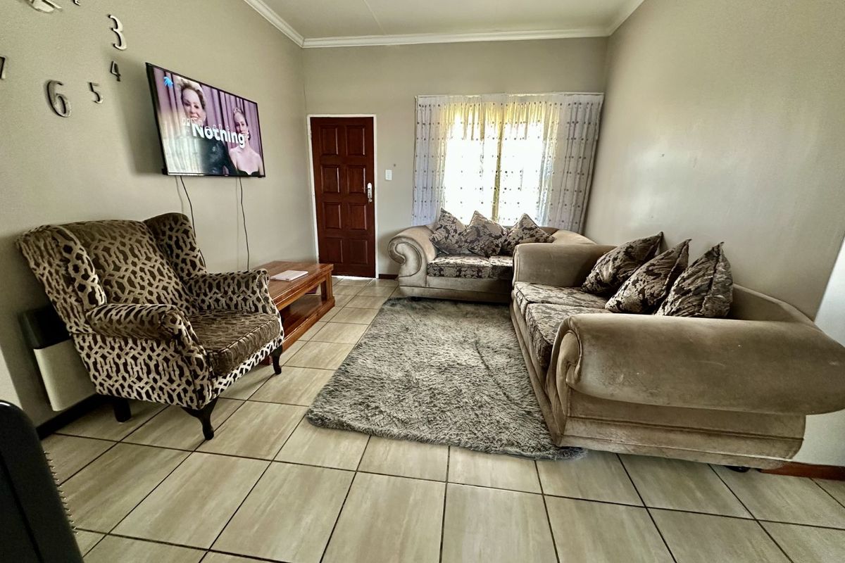 A living room featuring tiled flooring, a wall-mounted television, and a wooden door leading to an exterior area.