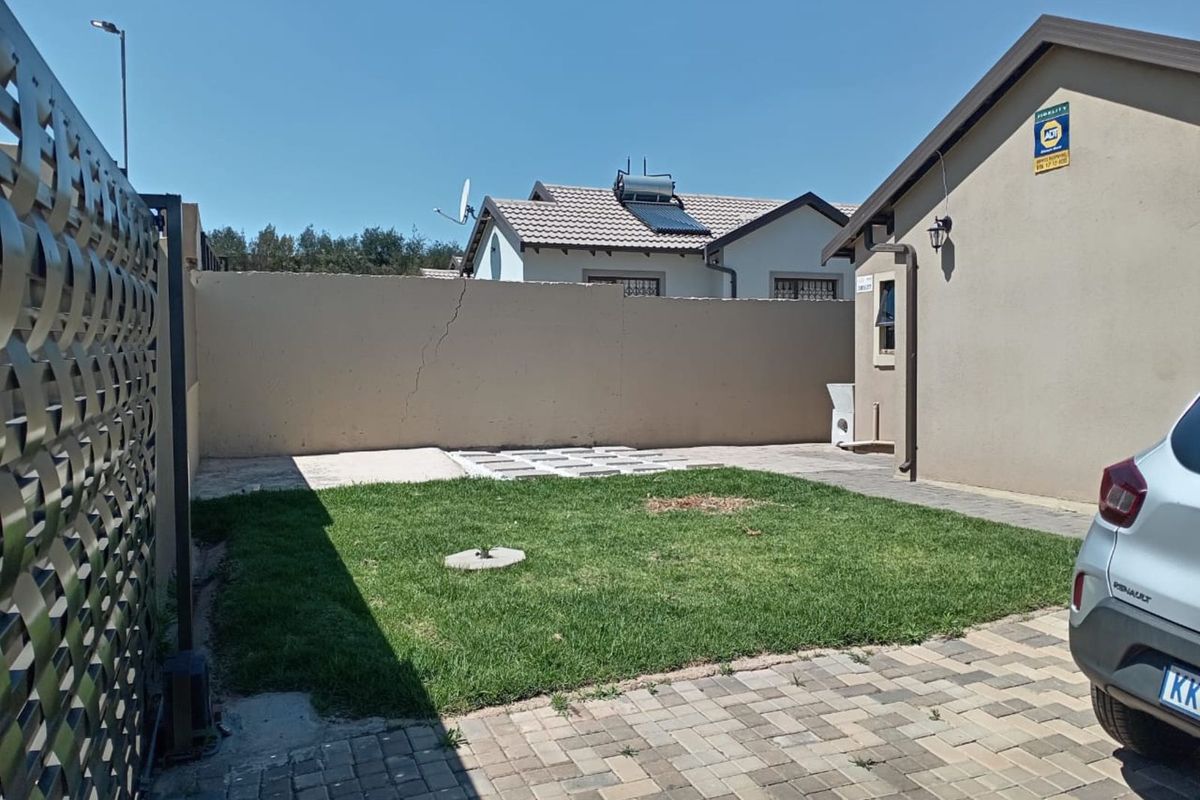A private rear garden area featuring a paved driveway, a small lawn, and a perimeter boundary wall with visible structural cracking.