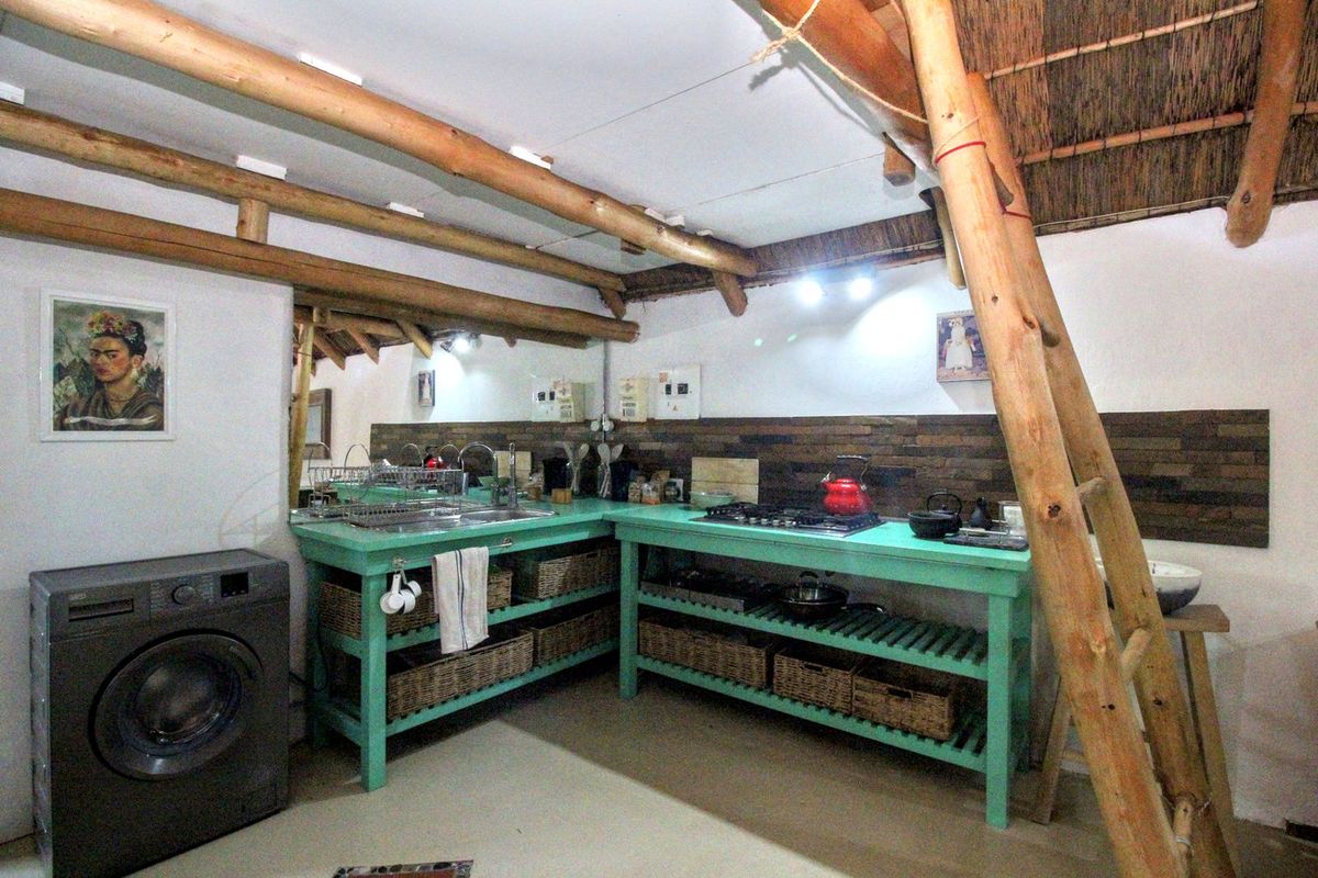 Rustic kitchen area featuring open timber shelving, integrated gas hob, stainless steel sink, and dedicated space for a front-loading washing machine.