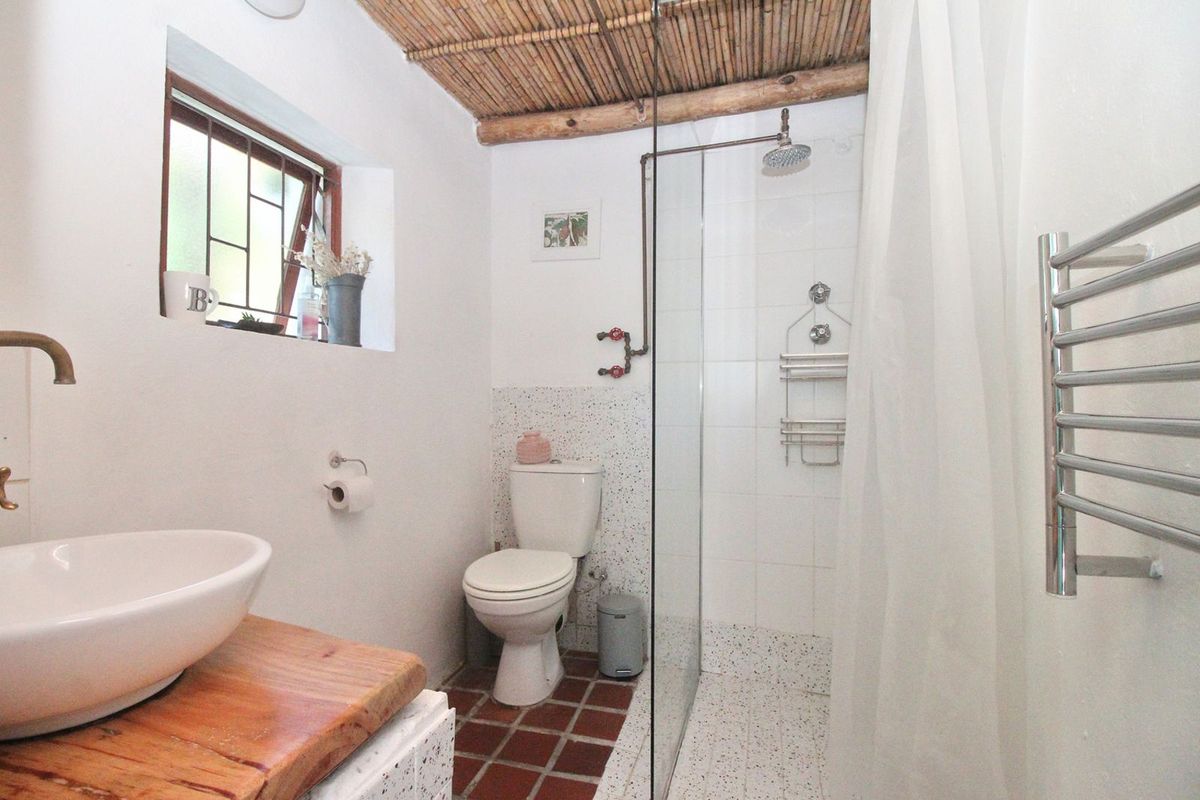 A compact bathroom featuring a walk-in shower with glass screen, vessel sink on a wooden vanity, and a heated towel rail.