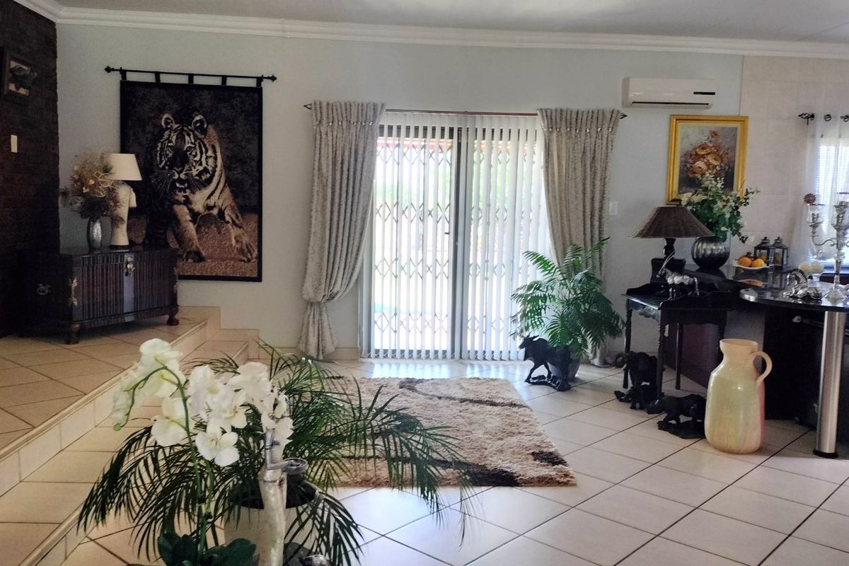 A spacious living area featuring tiled flooring, a split-system air conditioning unit, and sliding glass doors with security gates leading to the exterior.