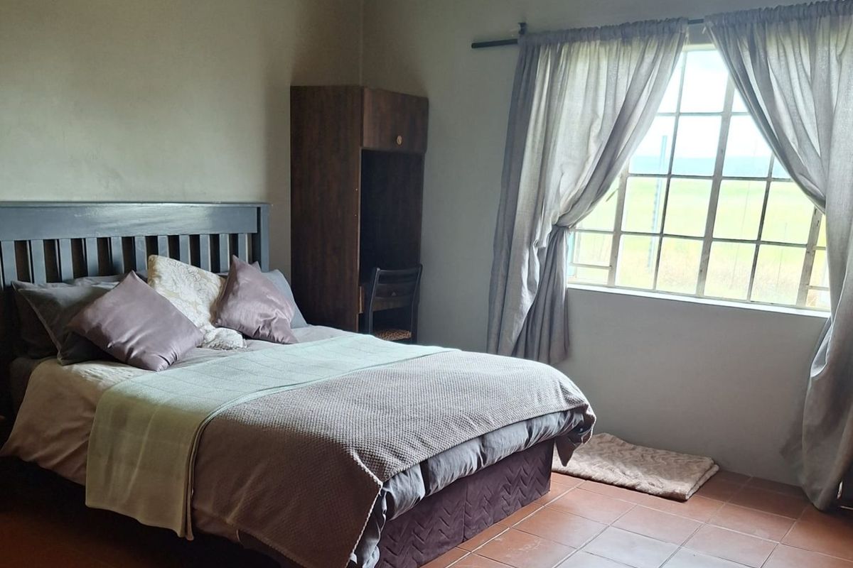 A bedroom featuring terracotta floor tiles, a large window with natural light, and neutral wall tones.