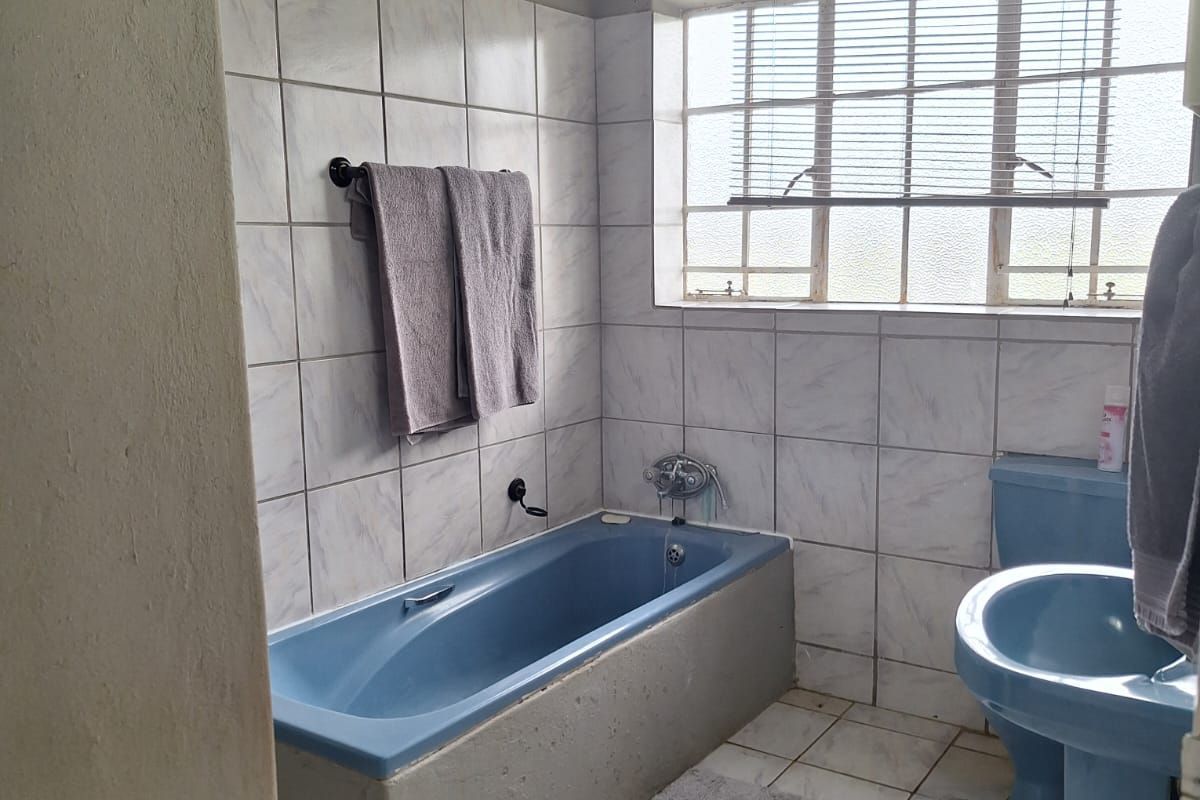 A dated bathroom featuring a blue bathtub, matching pedestal basin, and toilet, with tiled walls and flooring.