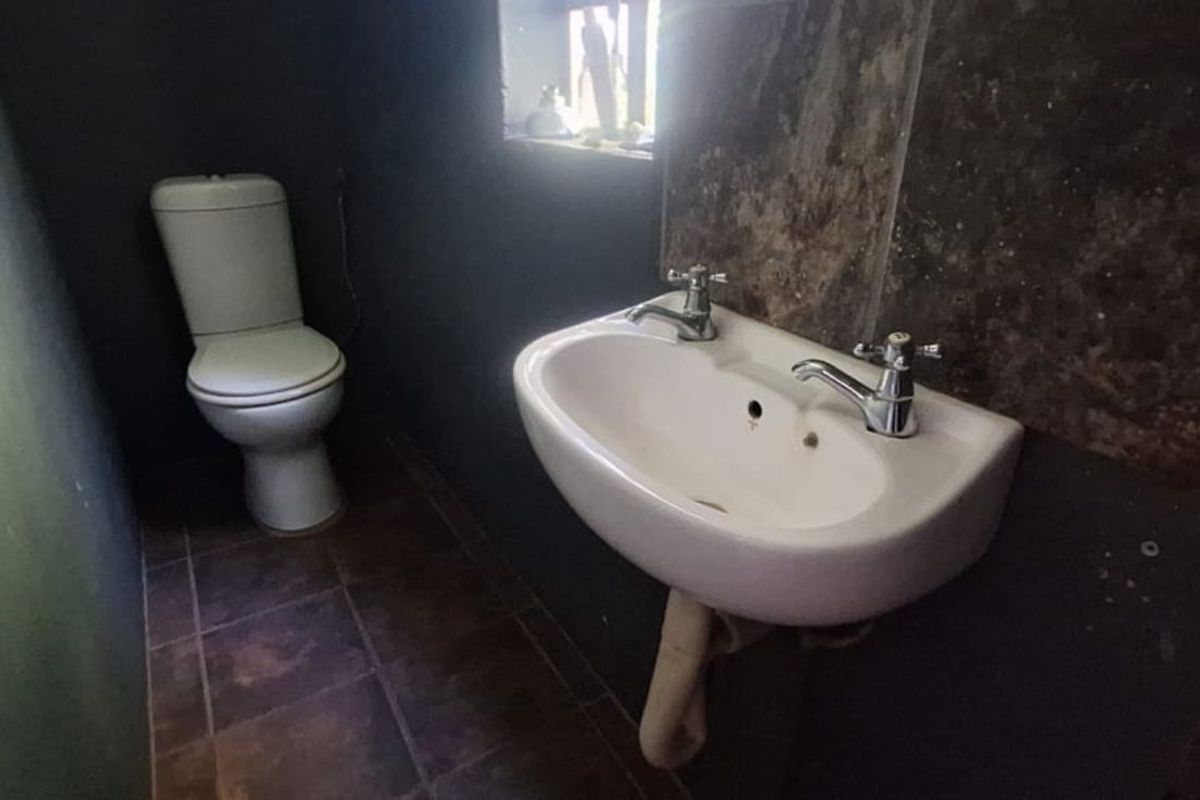 A compact bathroom featuring a wall-mounted basin with exposed plumbing and a standard toilet, finished with dark wall treatments and floor tiles.