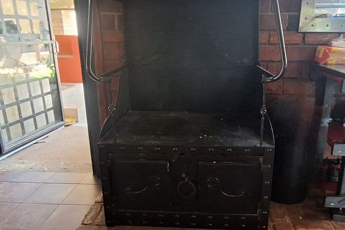 A rustic indoor fireplace featuring a black metal hearth and surround set against a brick wall, situated on a tiled floor.