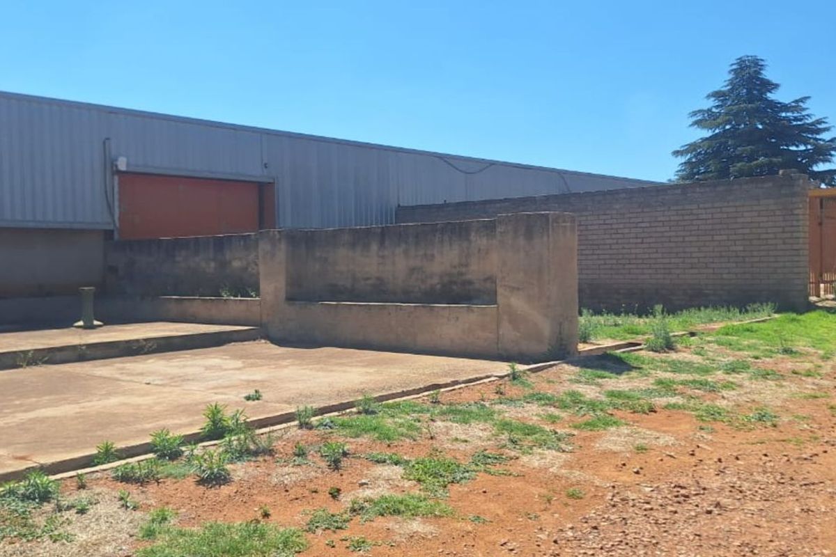 Exterior view of a farm utility area featuring concrete paving, masonry boundary walls, and a large metal-clad structure.