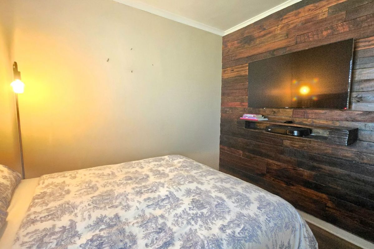 A bedroom featuring a rustic timber-clad feature wall with a mounted television and a floating shelf.