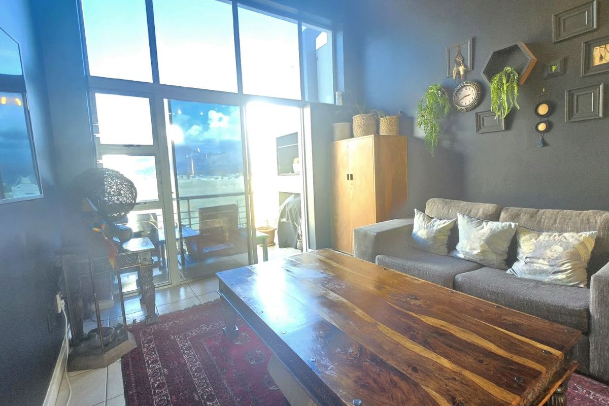 A bright living room featuring floor-to-ceiling windows and sliding glass doors that provide access to an attached balcony.