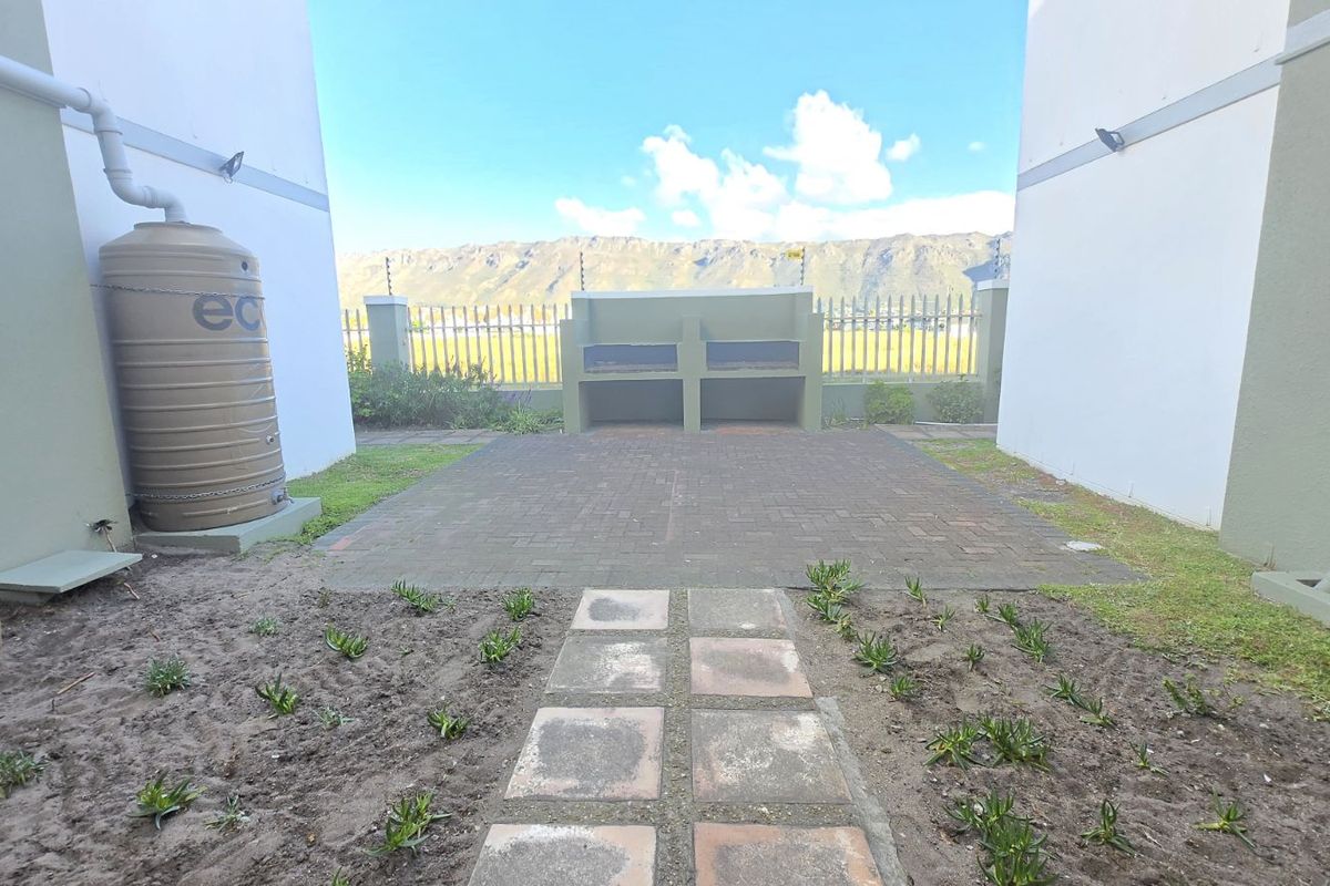 A private rear courtyard featuring a paved patio area with a built-in braai, water storage tank, and mountain views.