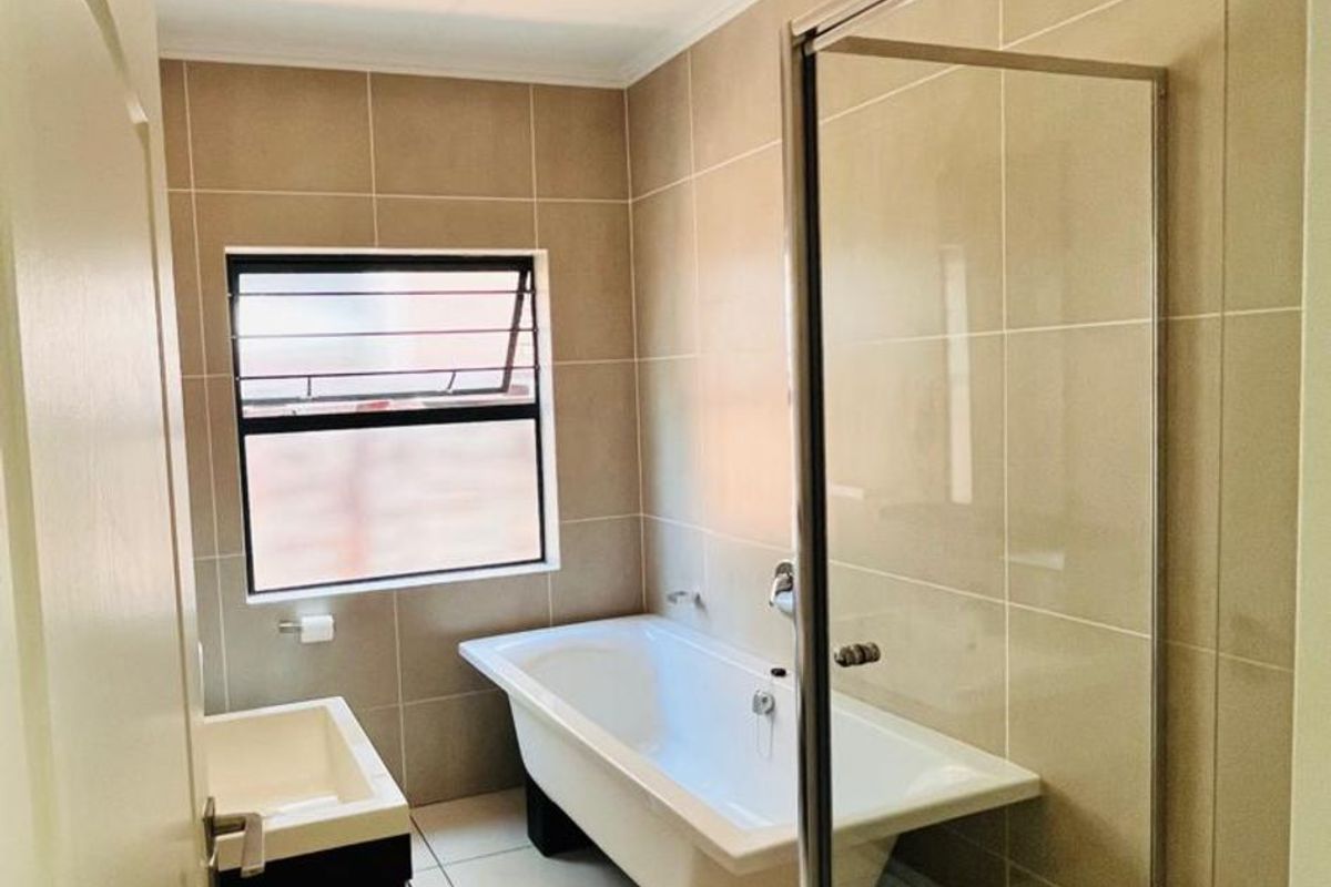 Modern bathroom featuring a freestanding bathtub, a separate glass-enclosed shower, and a wall-mounted vanity unit with neutral floor-to-ceiling tiling.