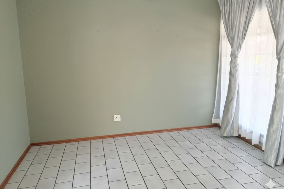 A bright, empty bedroom featuring neutral green walls, tiled flooring, and large windows with installed curtain tracks.