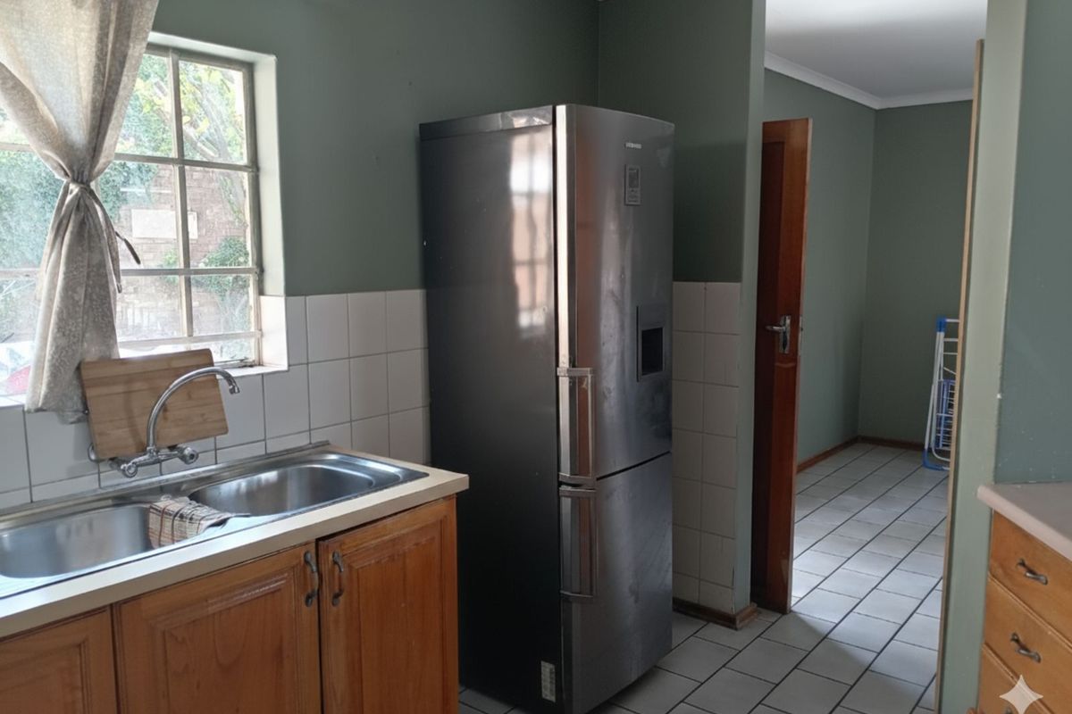 A functional kitchen area featuring wooden cabinetry, a double basin sink, and tiled flooring, leading into an adjacent living space.