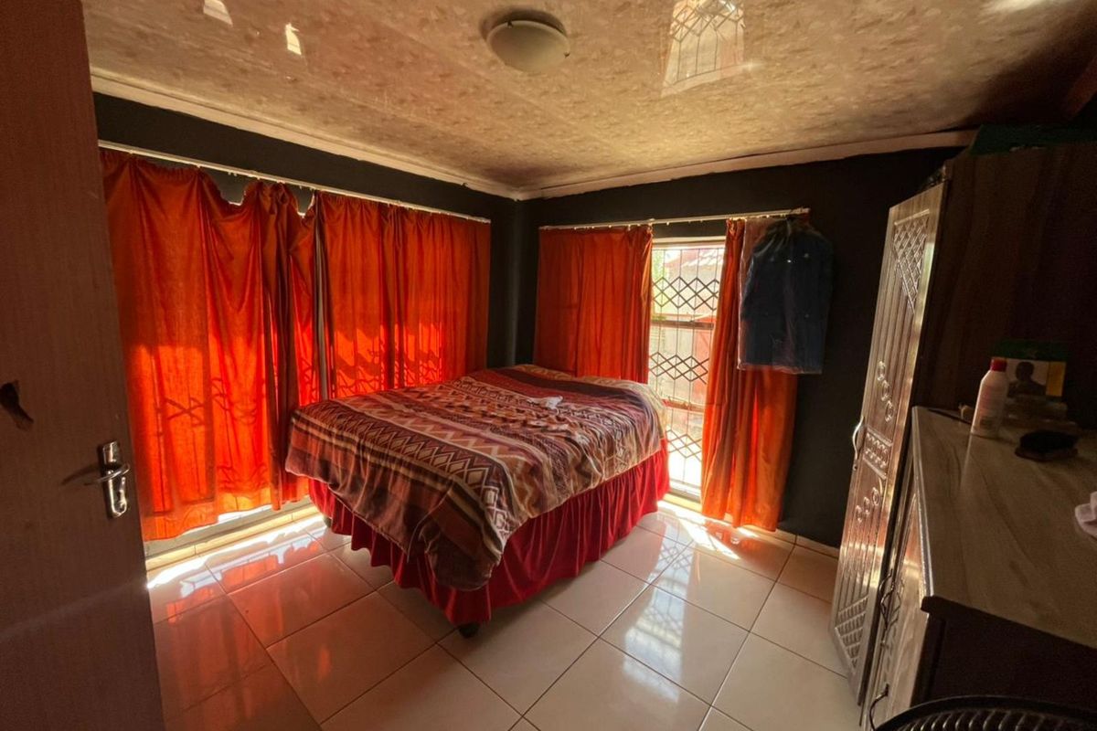 A bedroom featuring tiled flooring, security bars on windows, and a textured ceiling finish.