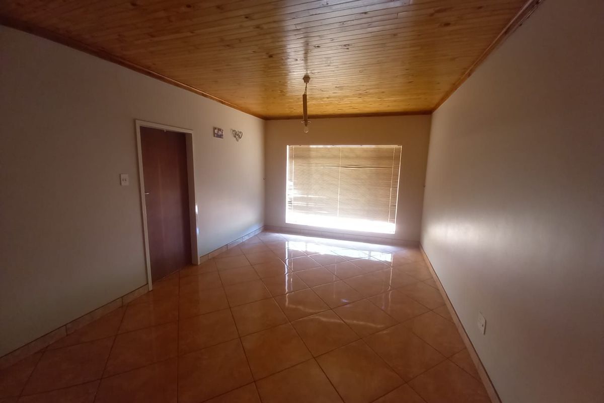 A bright, empty living room featuring polished ceramic floor tiles and a warm timber-paneled ceiling with a central light fixture.