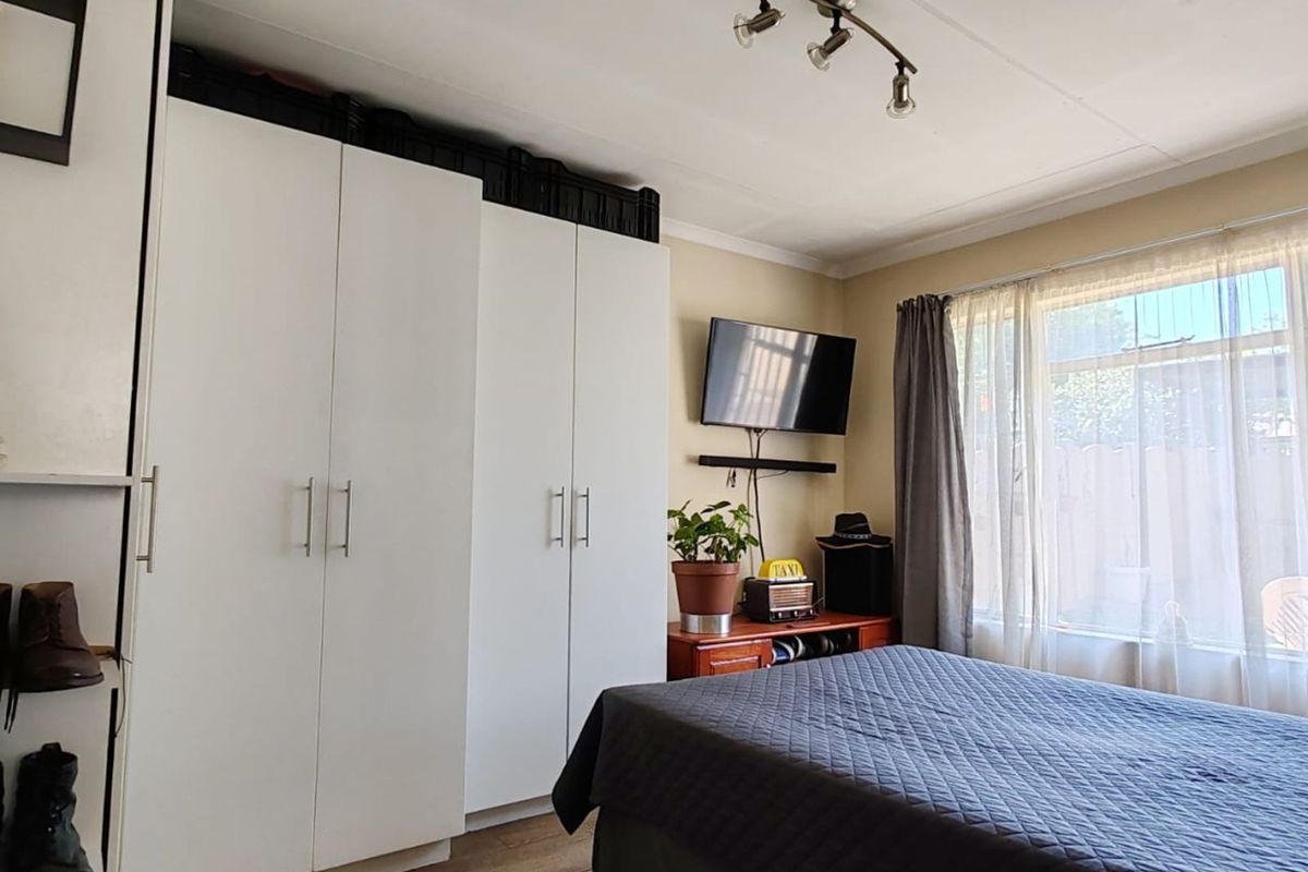 A functional bedroom featuring built-in white cabinetry, wood-look flooring, and natural light through a large window.