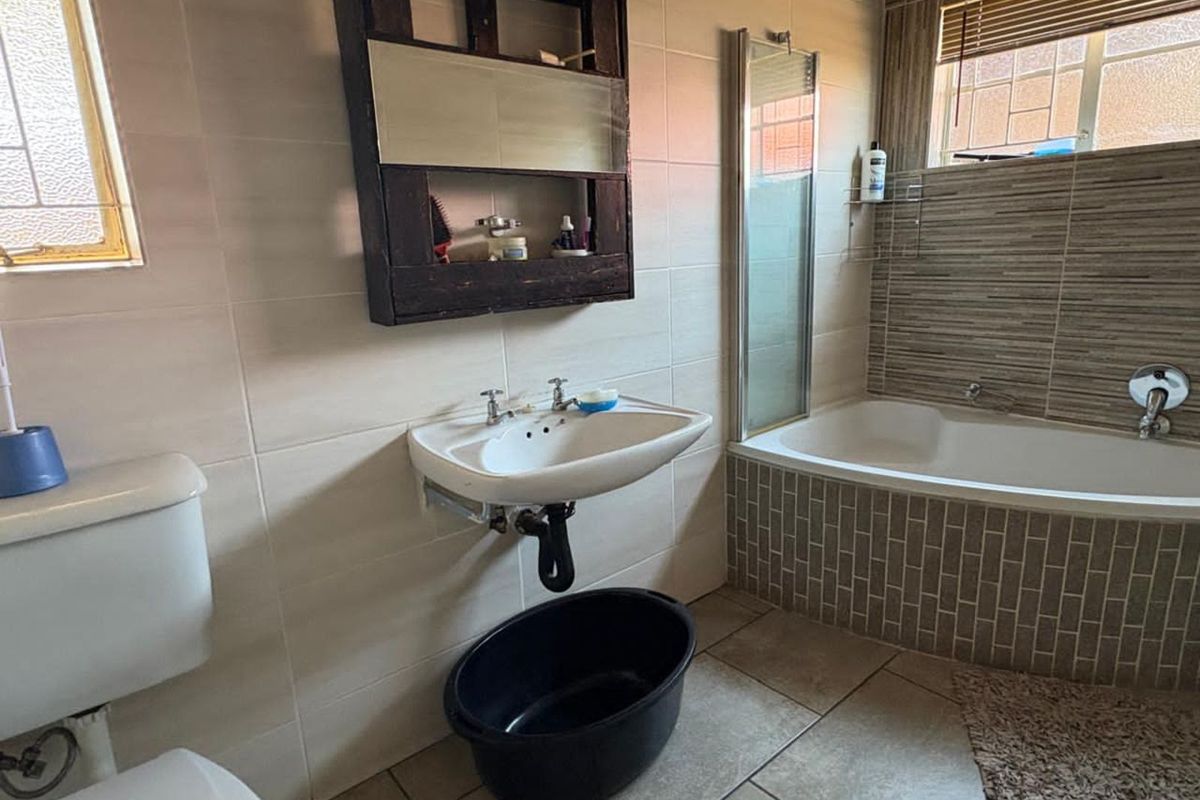 A functional bathroom featuring a wall-mounted basin, a bathtub with tiled surround, and neutral wall and floor tiling.