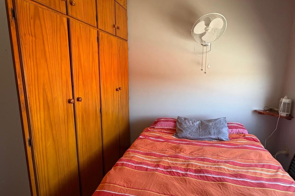 A compact bedroom featuring floor-to-ceiling wooden built-in cupboards and a wall-mounted fan.
