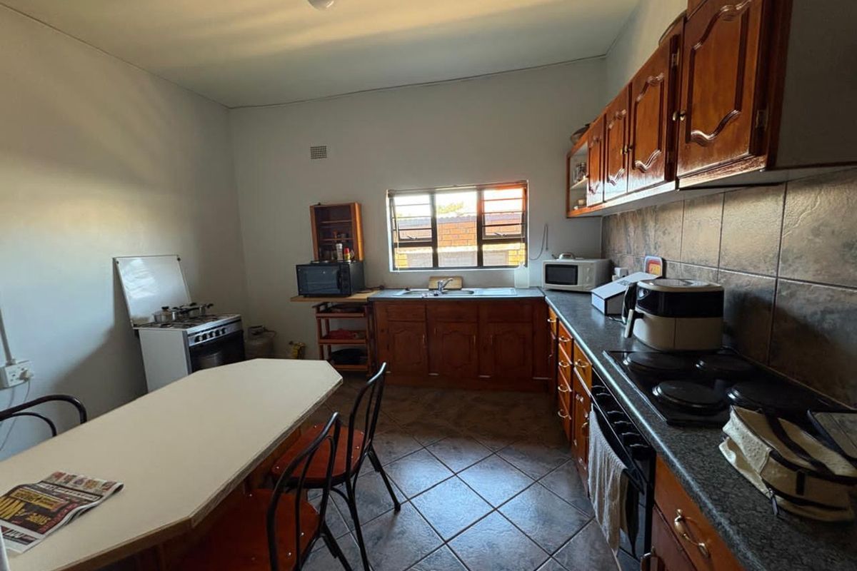 A functional kitchen featuring wooden cabinetry, tiled flooring, a built-in stove, and a window providing natural light.