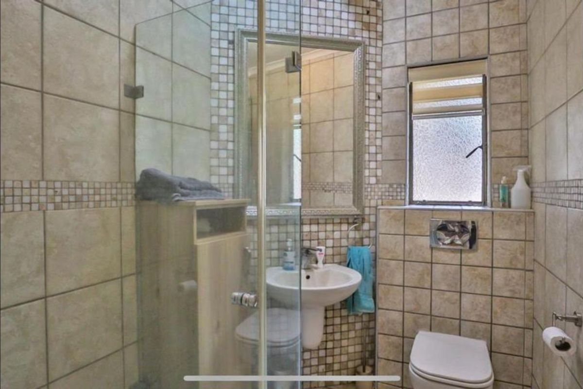 Compact bathroom featuring a glass-enclosed shower, pedestal basin, and wall-mounted toilet with neutral tiled walls and mosaic accents.