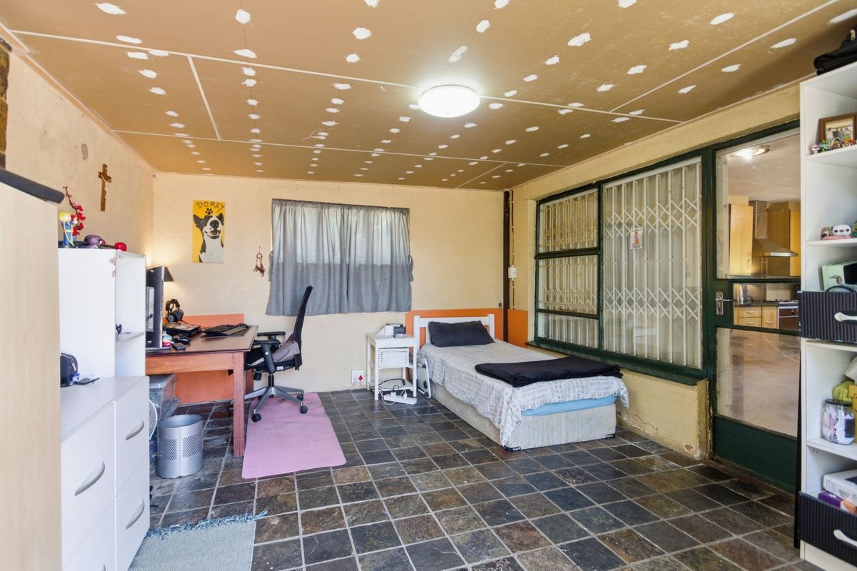 A bedroom featuring slate-style floor tiles, a large window with security gate, and an unfinished ceiling, offering potential for renovation.
