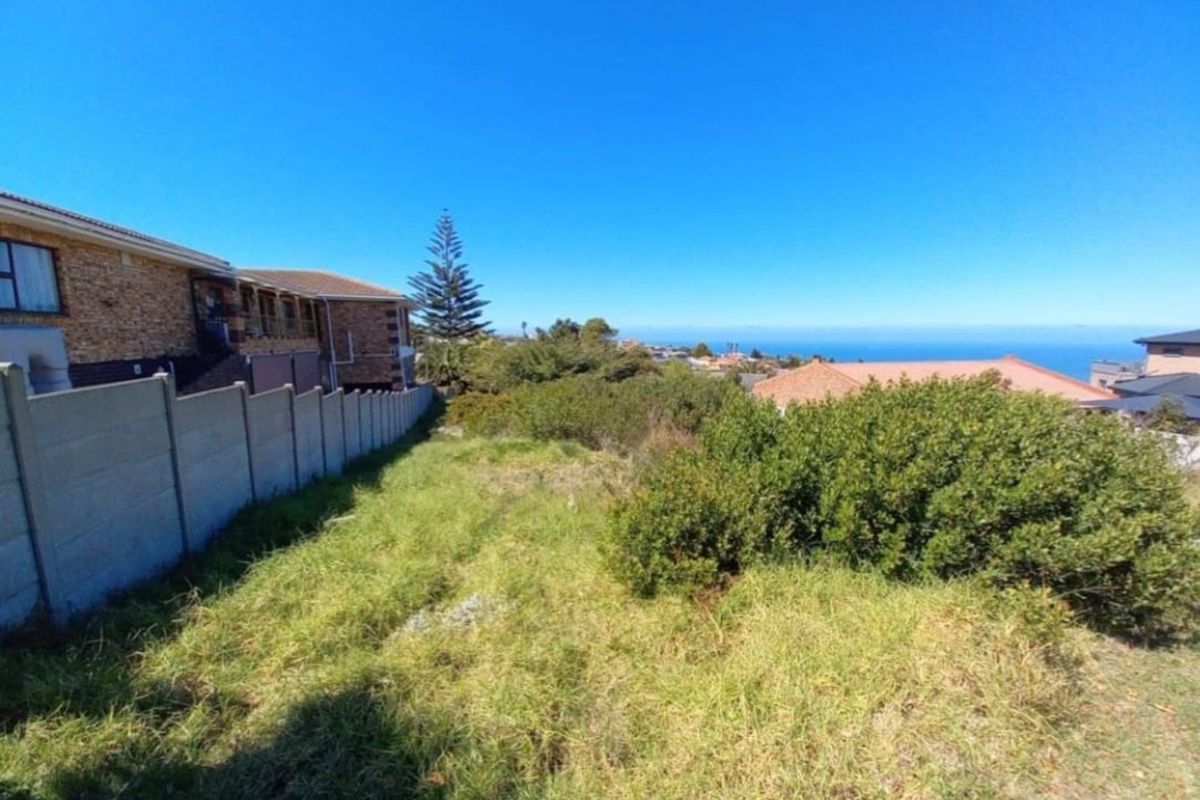 A vacant residential plot featuring natural vegetation, a boundary wall, and scenic coastal views in a established neighborhood setting.