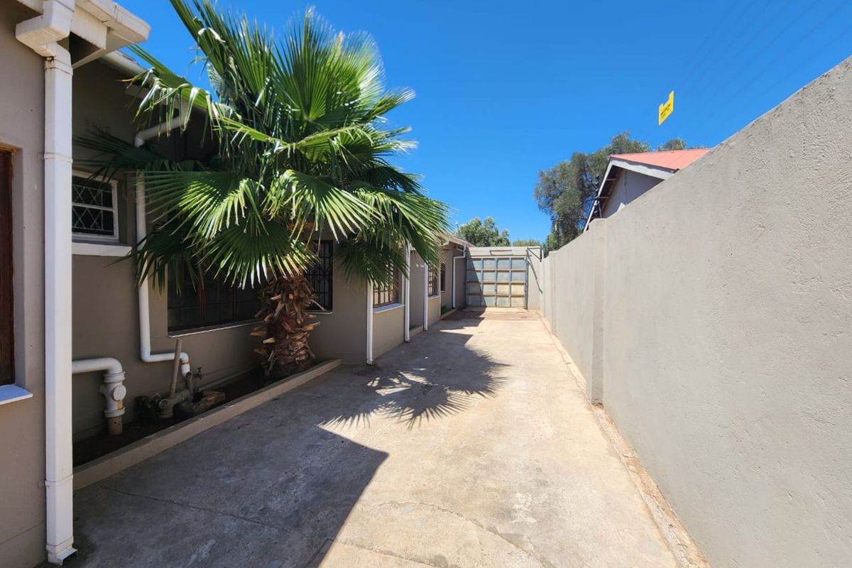 A side exterior view of the property featuring a concrete driveway, boundary wall, and access to the rear garage area.