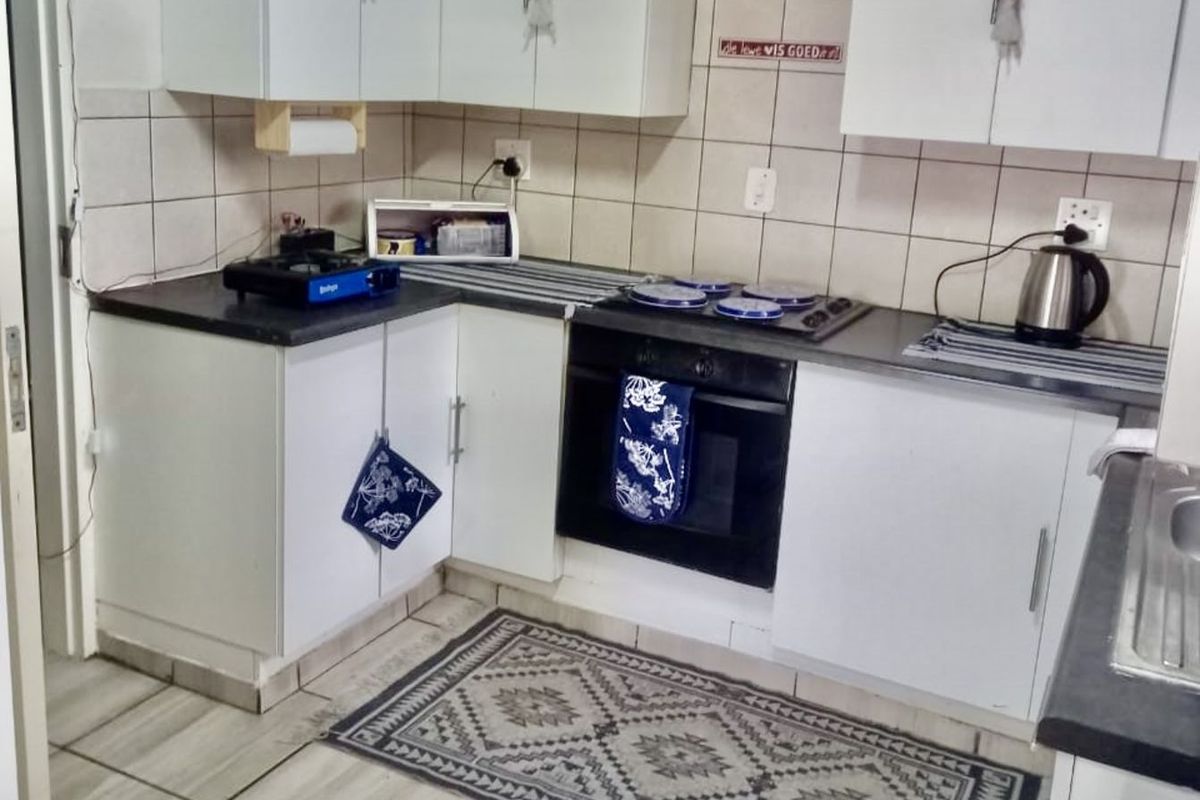 Compact kitchen featuring white cabinetry, dark countertops, built-in oven, and extractor fan with tiled splashback and flooring.