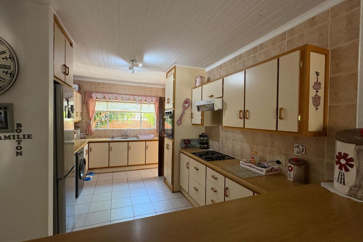 A functional kitchen featuring built-in cabinetry, a gas hob, an integrated oven, and tiled flooring with a view towards the rear garden.