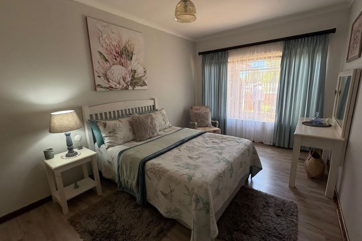 A well-maintained bedroom featuring laminate flooring, curtain rails, and a window with security bars.