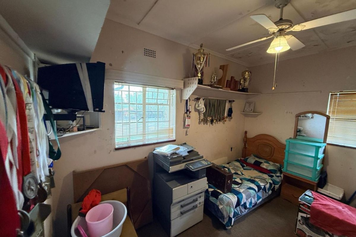 A bedroom featuring a ceiling fan, built-in shelving, and security bars on the windows, currently requiring cosmetic updates and repairs to walls and ceilings.