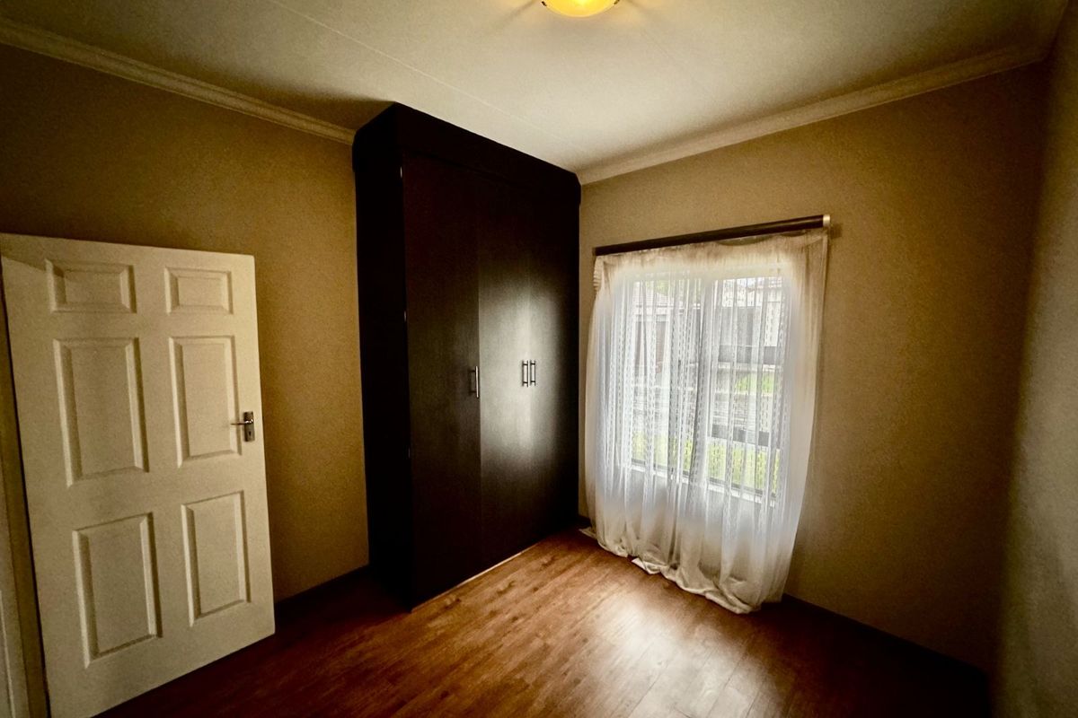 A bedroom featuring dark built-in cabinetry, laminate flooring, and a window with sheer curtains.