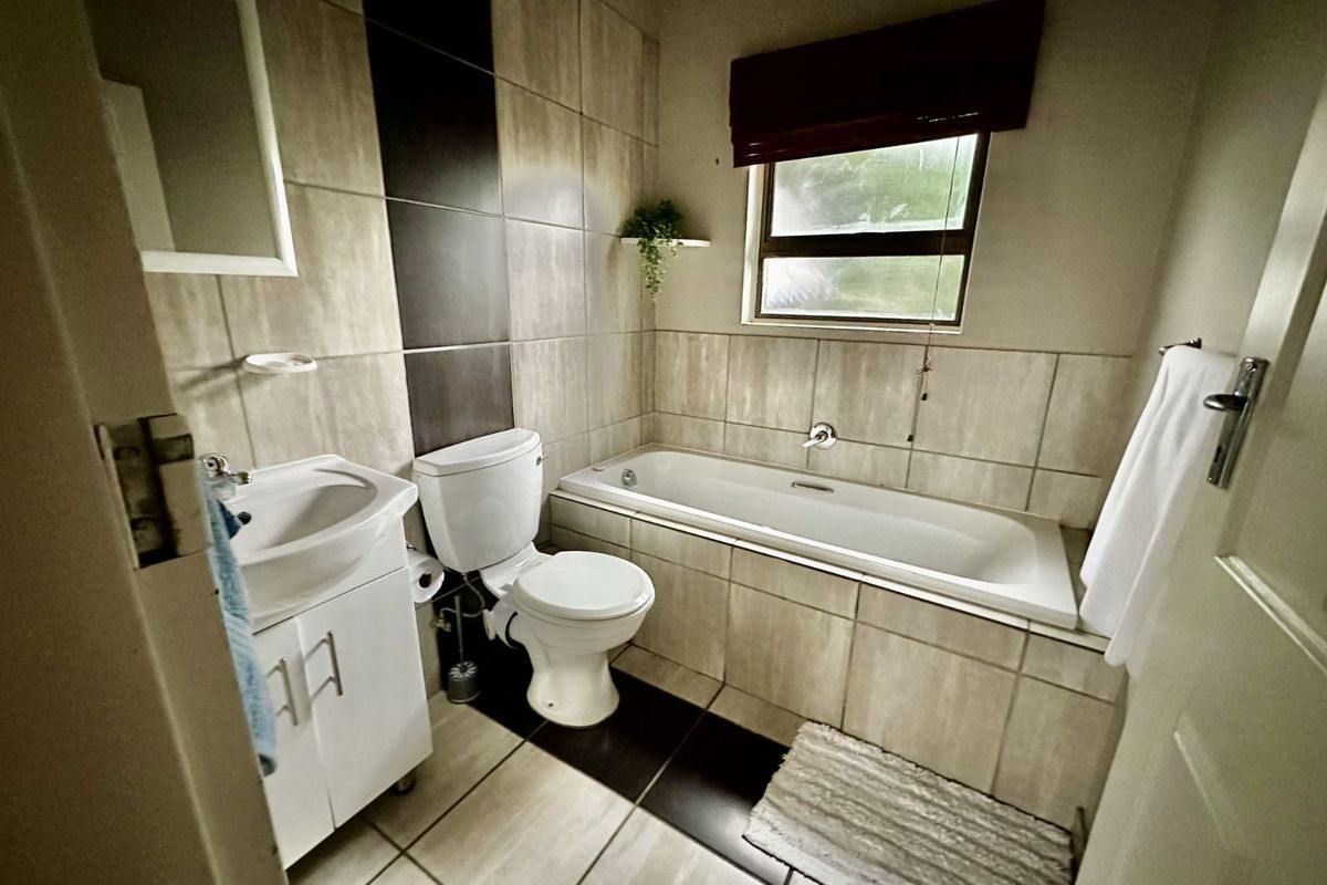 A compact bathroom featuring a built-in bathtub, a vanity basin, and a toilet, finished with neutral wall and floor tiling.