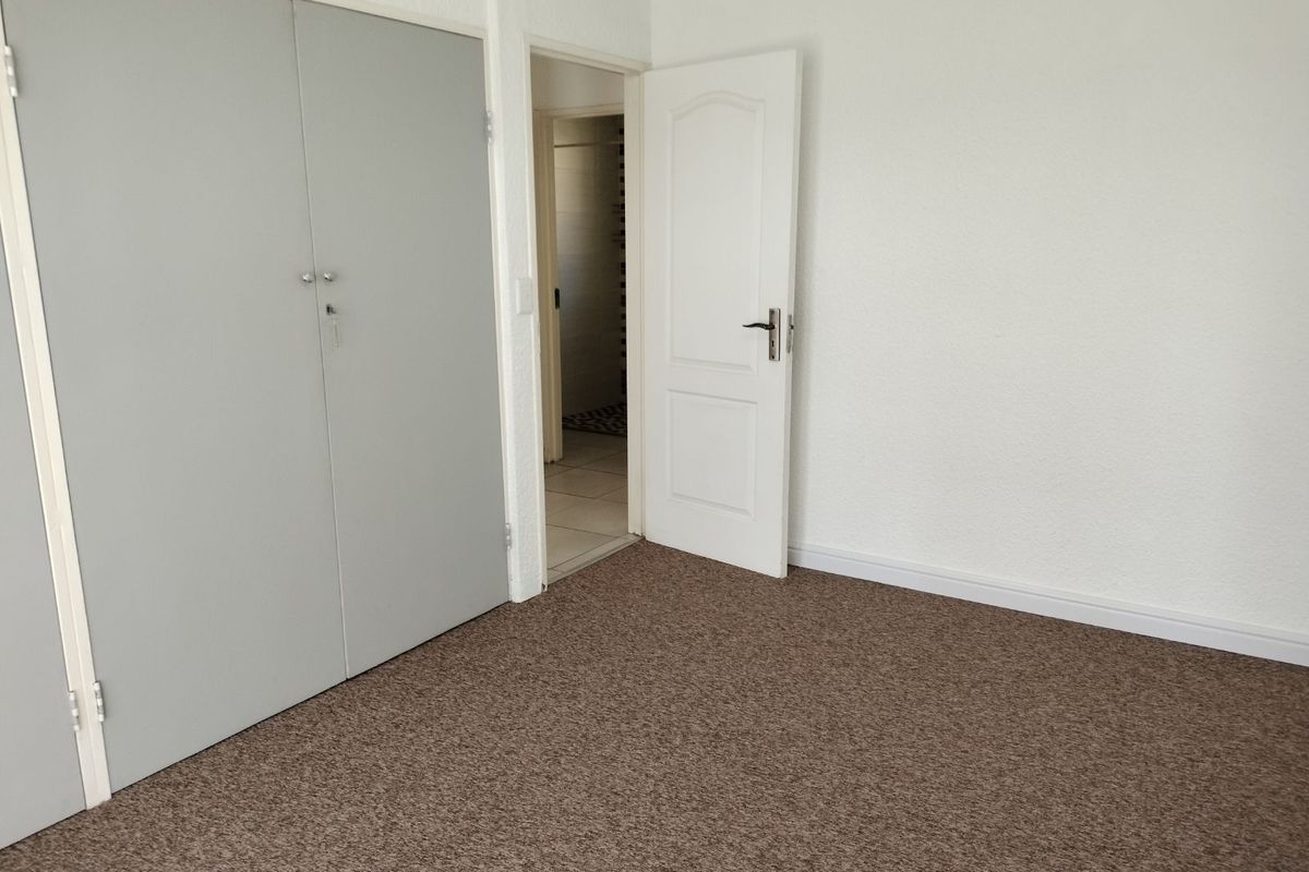 A clean, empty bedroom featuring neutral carpeting, built-in cupboards, and a doorway leading to an adjacent bathroom.