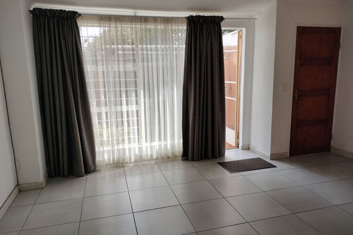 A bright living area featuring large glass sliding doors with curtains, tiled flooring, and direct access to an outdoor space.