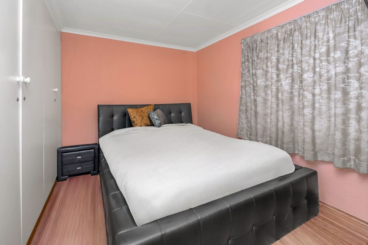A bedroom featuring built-in cupboards, wood-look flooring, and a window with curtain tracks.
