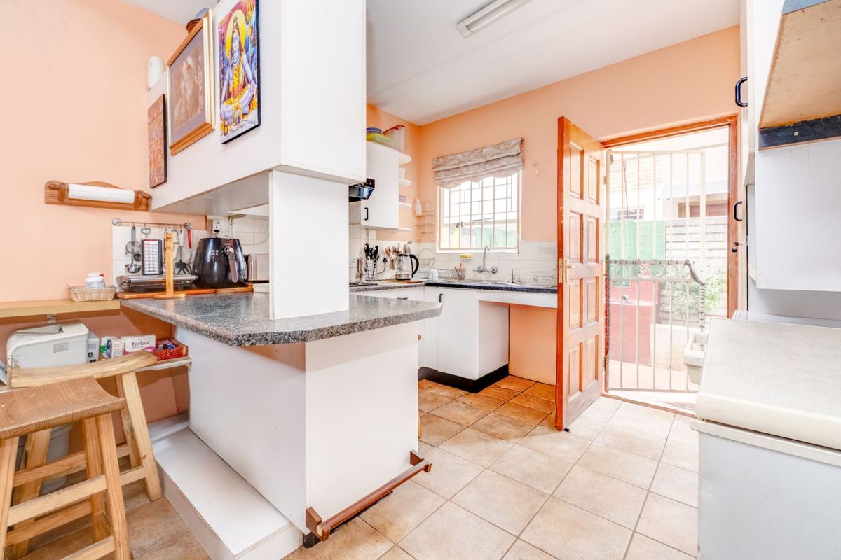 A functional kitchen featuring a breakfast bar, tiled flooring, and direct access to the rear exterior through a security gate.