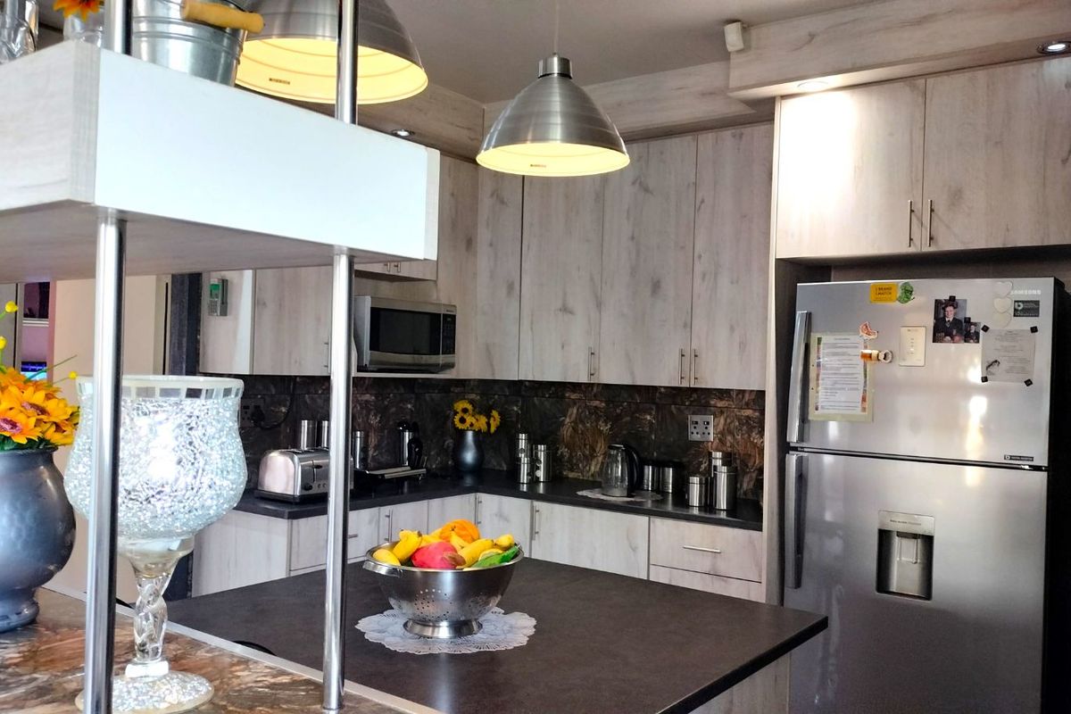 A functional kitchen featuring light wood-grain cabinetry, dark countertops, a built-in microwave, and modern pendant lighting over a central island workspace.