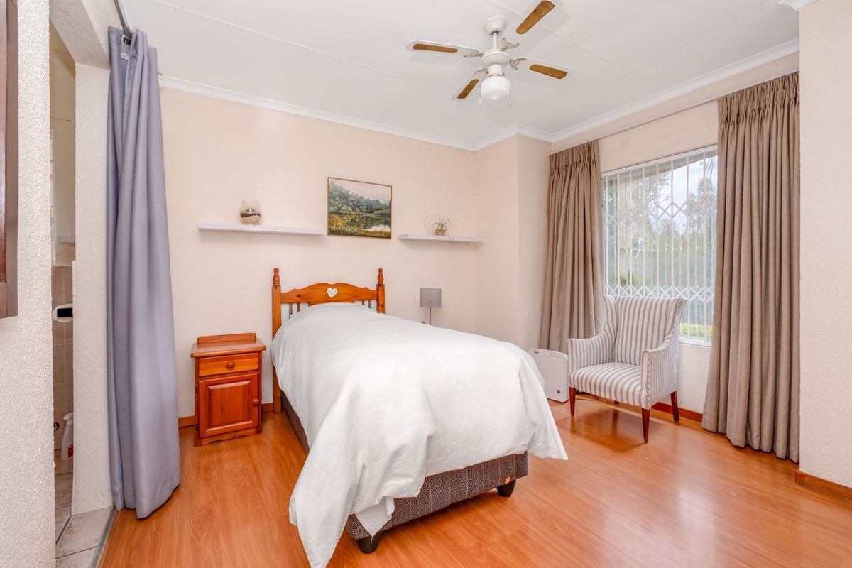 A bedroom featuring laminate flooring, a ceiling fan, and security bars on the window.