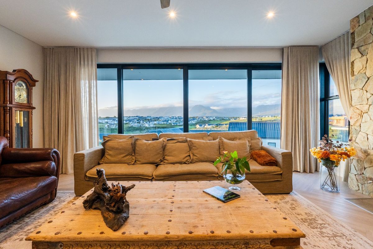A spacious living room featuring large floor-to-ceiling windows that frame expansive mountain and landscape views, complemented by a natural stone feature wall.